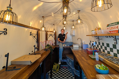 Inside the Frenchie’s Pizza horsebox with wooden counters, hanging lights and a team member preparing for service.