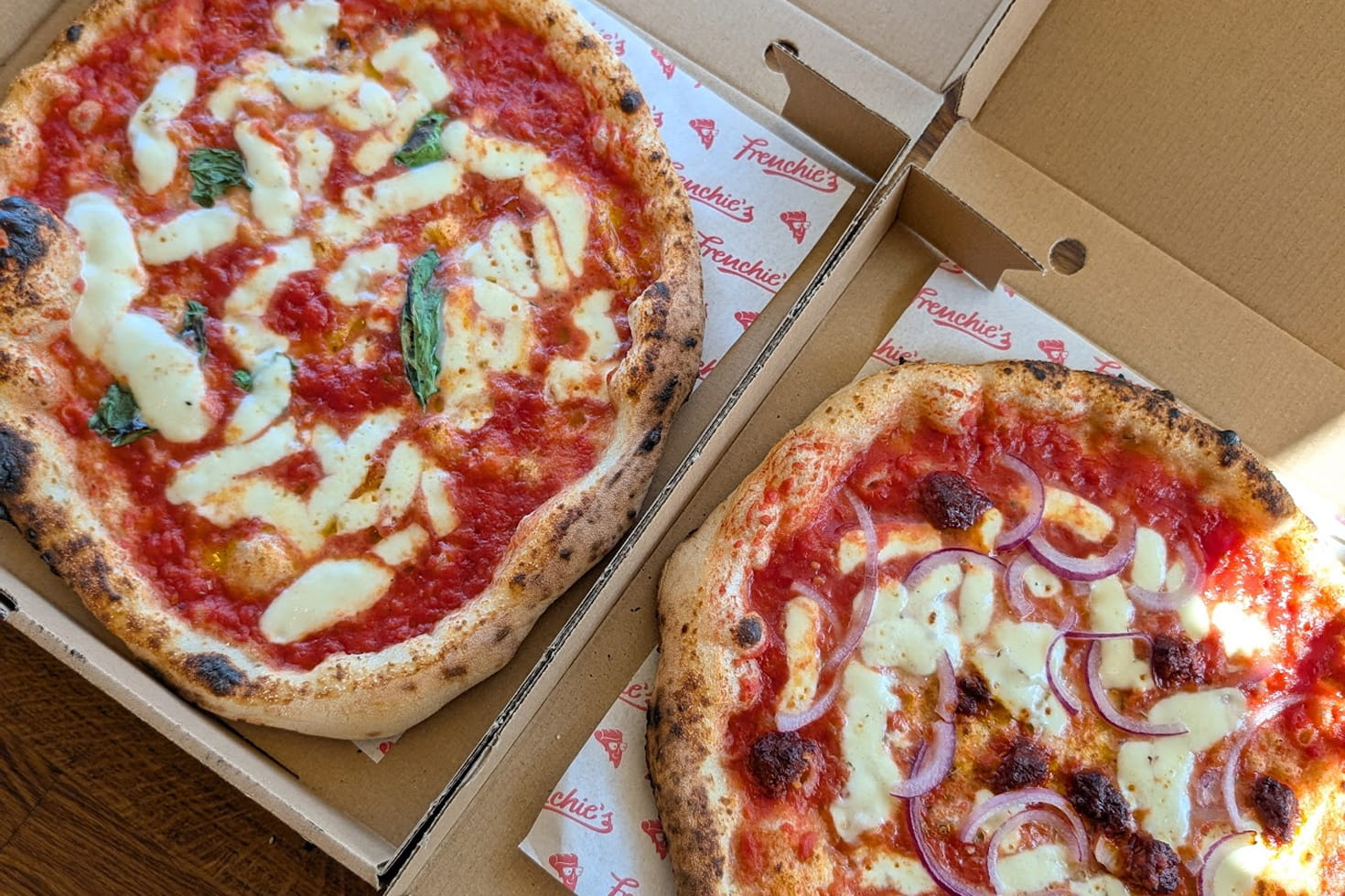 Two freshly baked Frenchie’s pizzas in takeaway boxes, including Margherita and ’nduja with red onion.