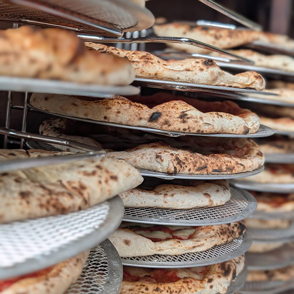 Multiple pizzas stacked on metal racks with browned and bubbly crusts, some with visible toppings.