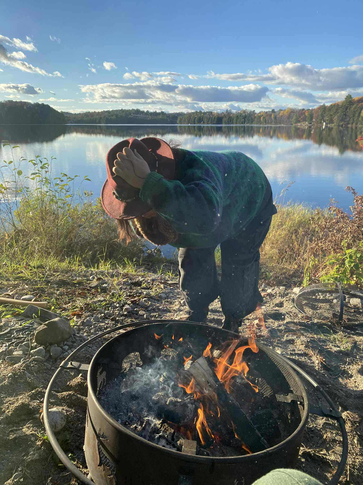 Amanda tending to a campfire in front of a peaceful lake on a fall afternoon.
