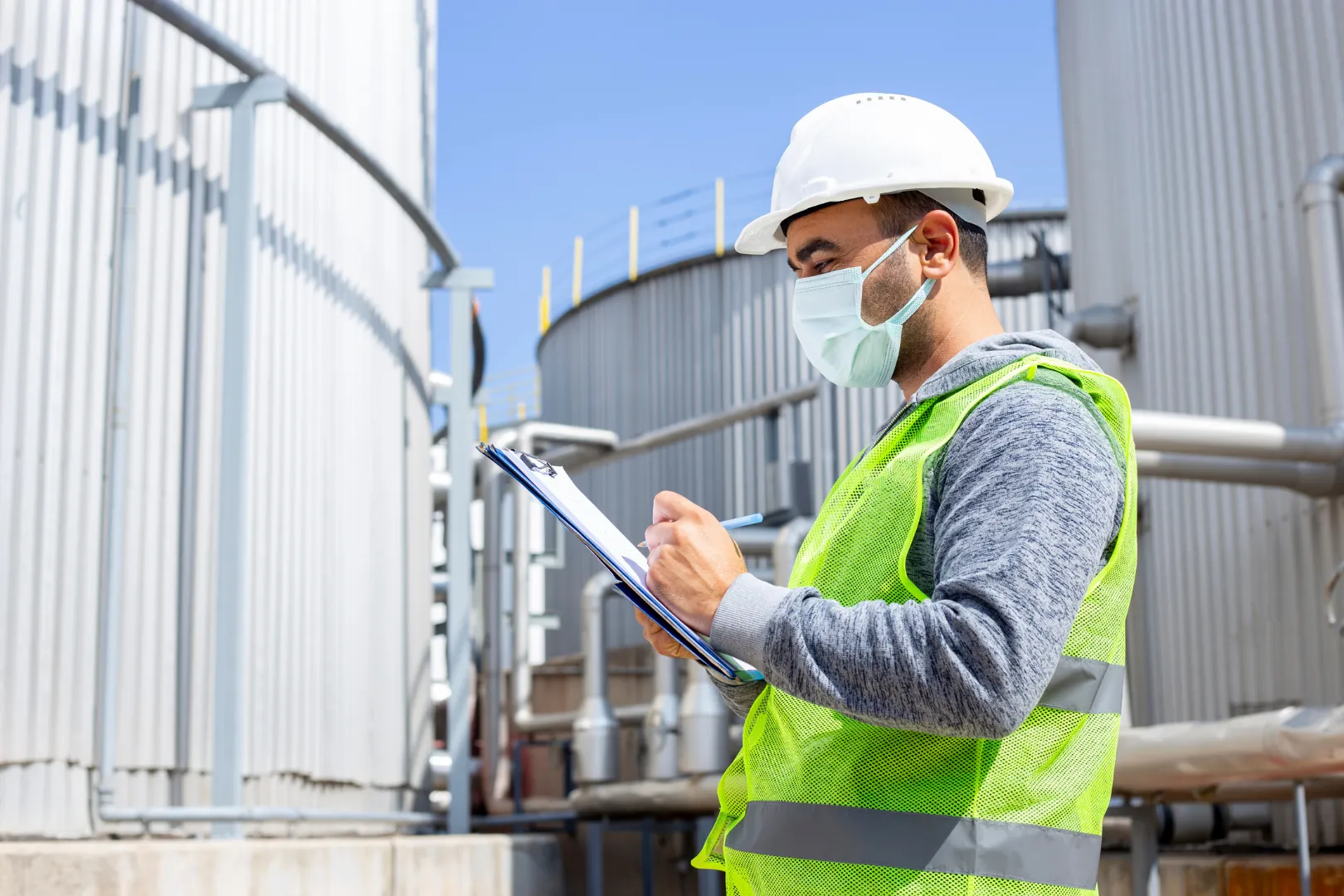Mann mit gelber Warnweste und Klemmbrett vor Industriegelände