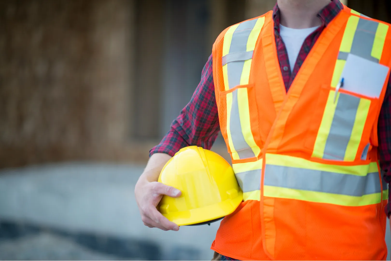 Mann mit oranger Warnweste hält gelben Schutzhelm unter dem Arm
