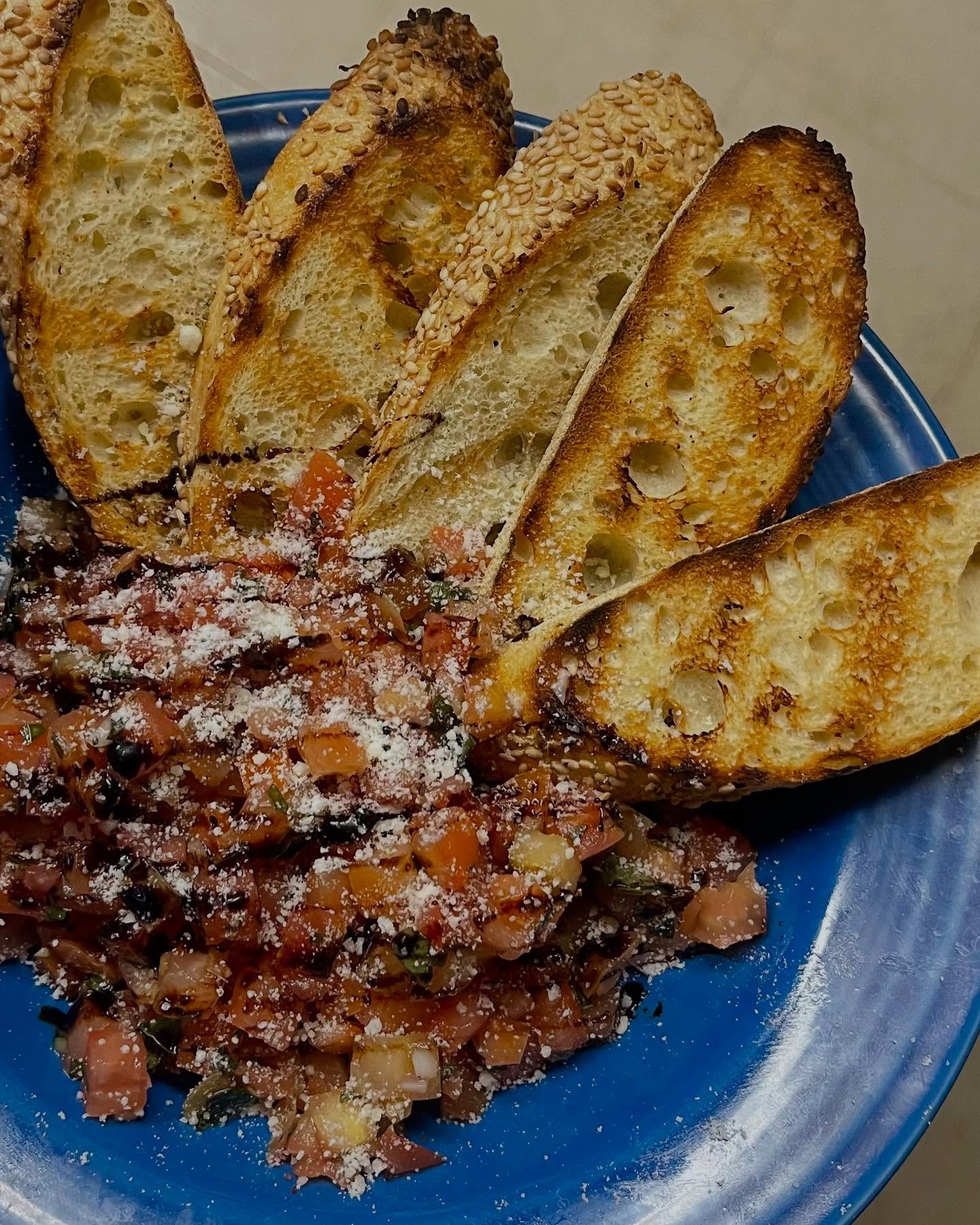 A blue plate featuring slices of bread served with fresh tomato salad, topped with cheese.