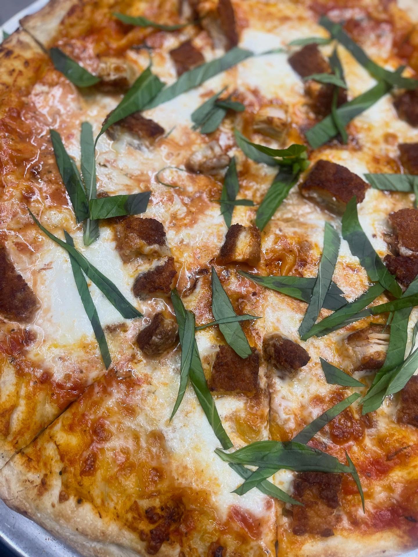 A pizza topped with melted cheese, meat and fresh green leaves,