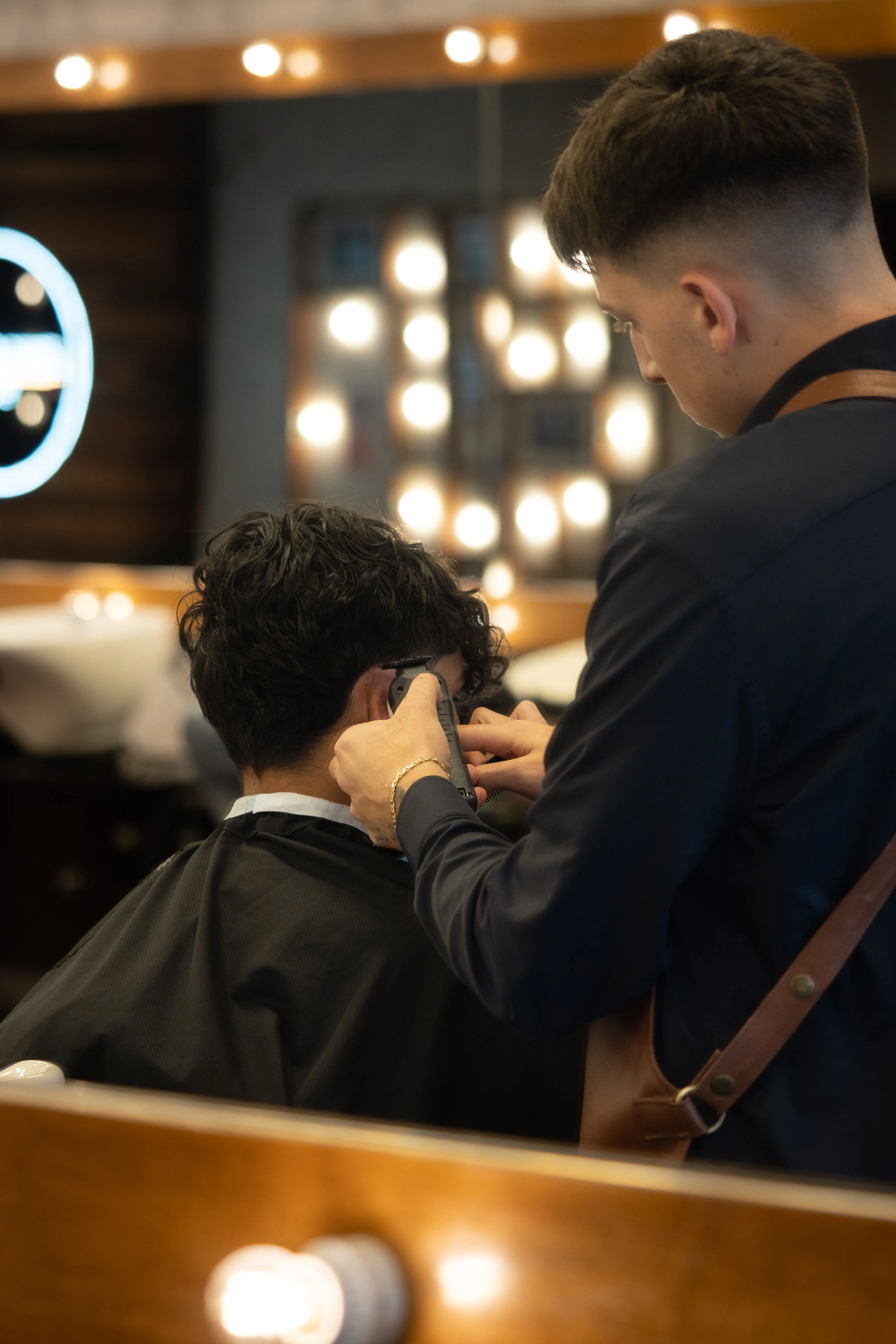 A barber uses clippers to give a precise fade to the back of a client's head.