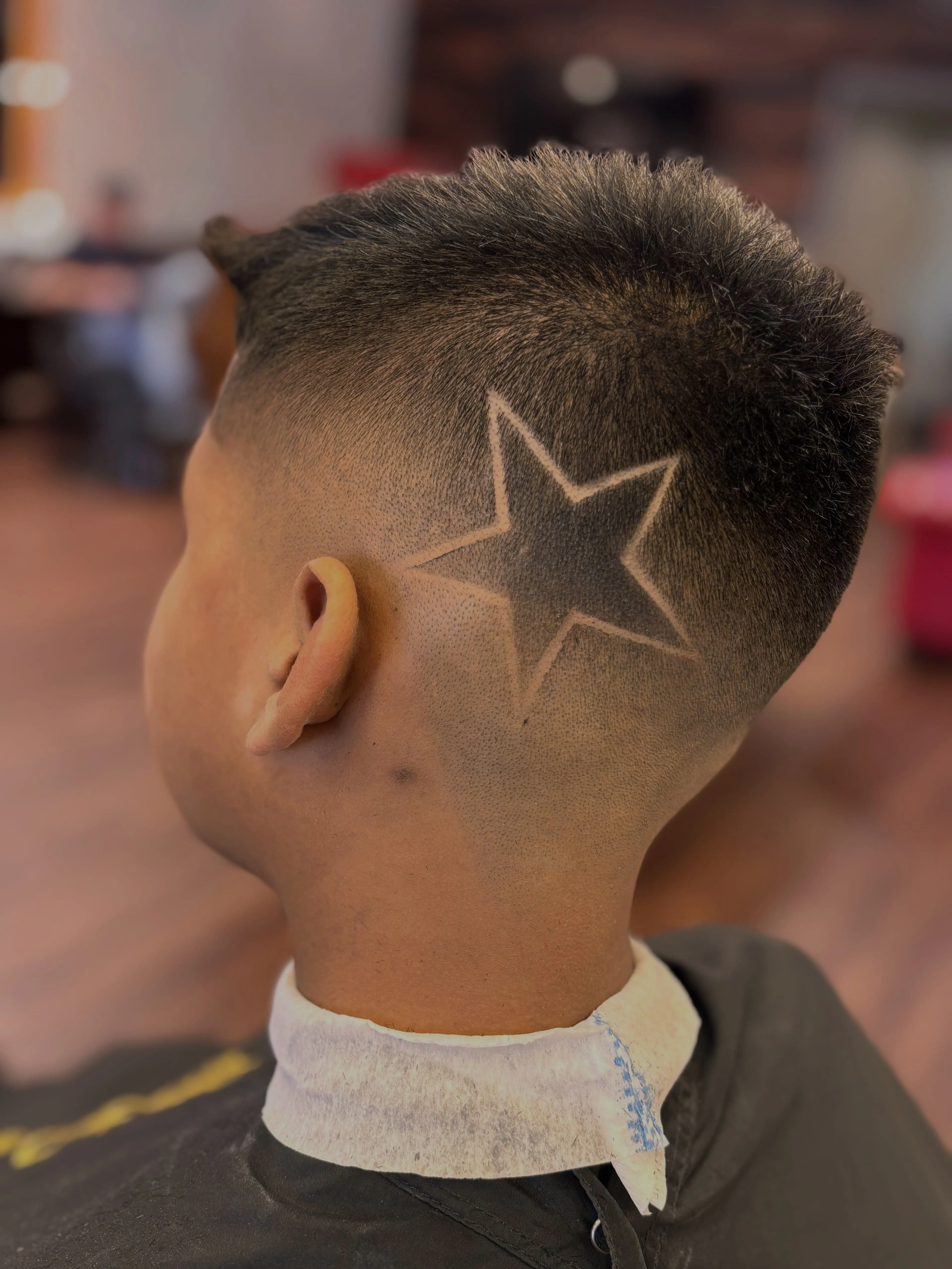 A sharp fade haircut features a detailed five-point star design carved into the back of the head.