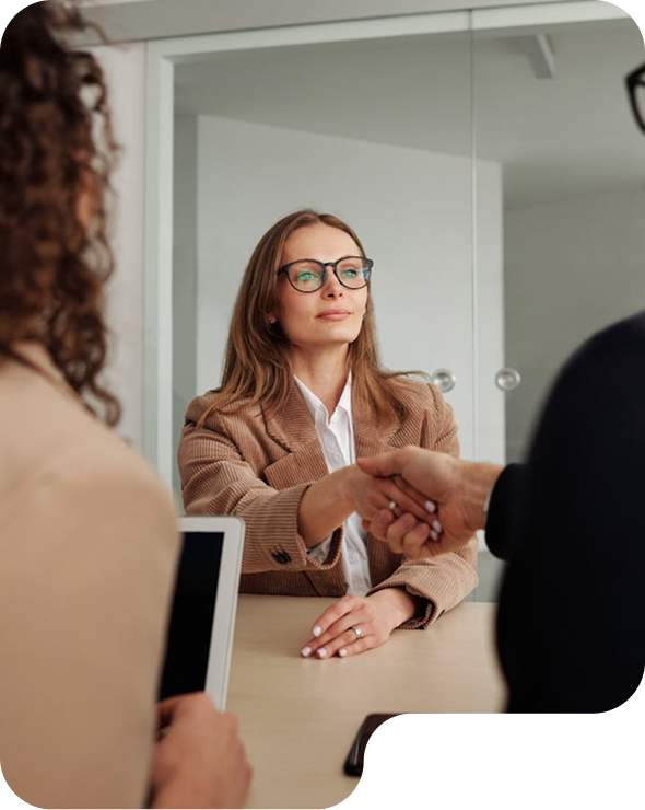 Mujer con gafas y chaqueta marrón dando la mano a alguien durante una reunión en una oficina.