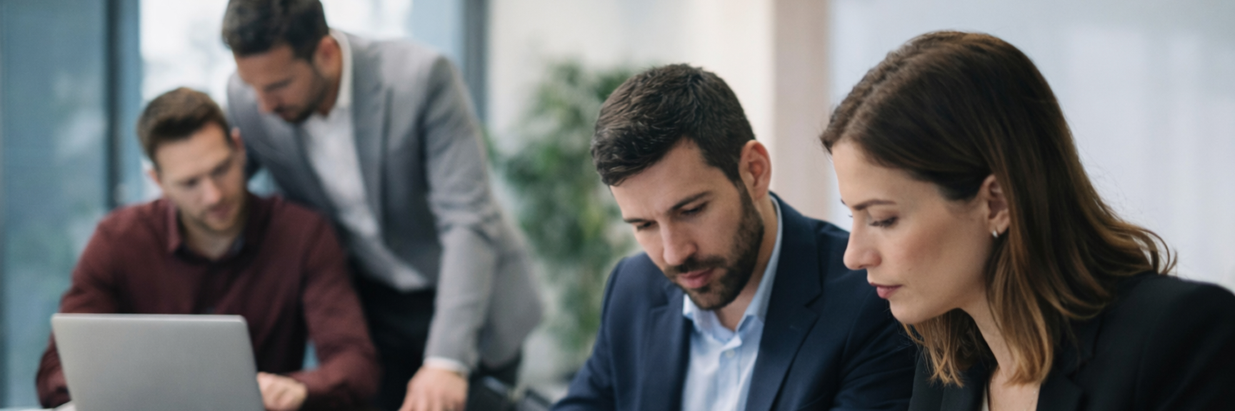 Cuatro profesionales trabajando juntos en una oficina moderna, revisando documentos y usando una laptop.