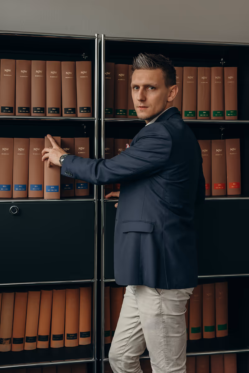 Mann im dunklen Blazer greift nach einem Buch in einem Bücherregal mit juristischen Büchern.