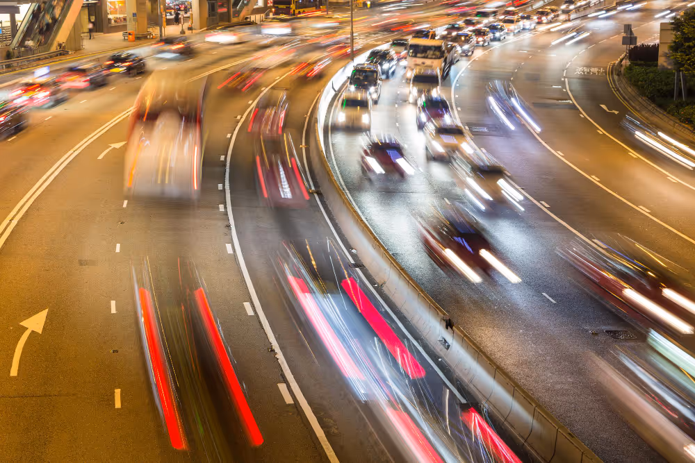 Nachtaufnahme einer mehrspurigen Autobahn mit verschwommenen Lichtern von fahrenden Autos und Bussen in Bewegung.