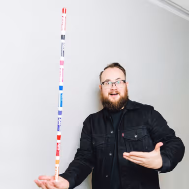 Will smiling and gesturing while holding a tall stack of colorful markers