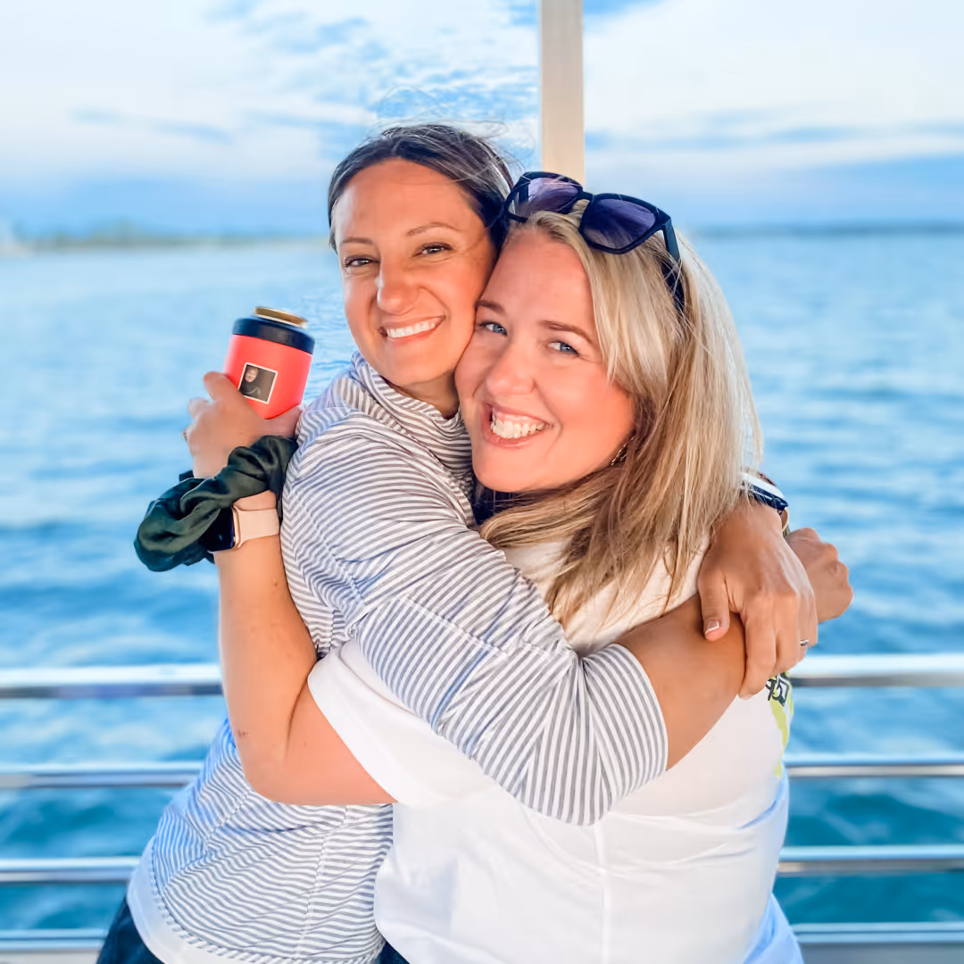 Two friends hugging and smiling on a boat with water in the background