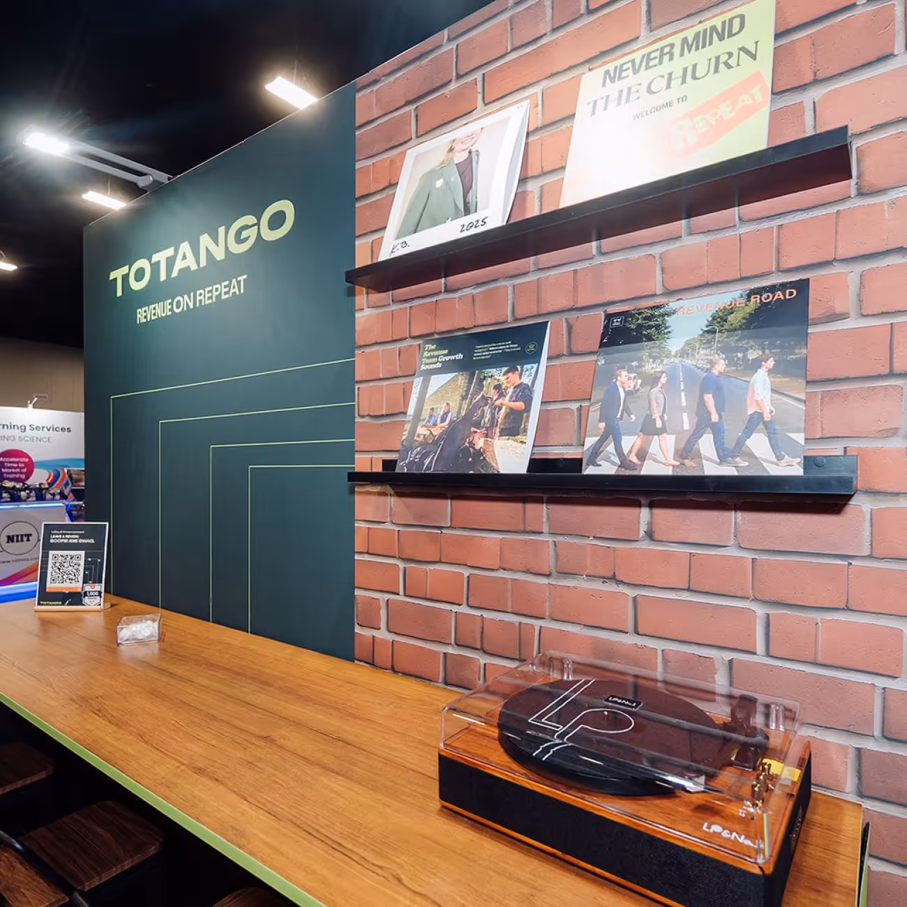 Totango booth with a brick wall holding vinyl records and a wooden table with a vinyl record player.