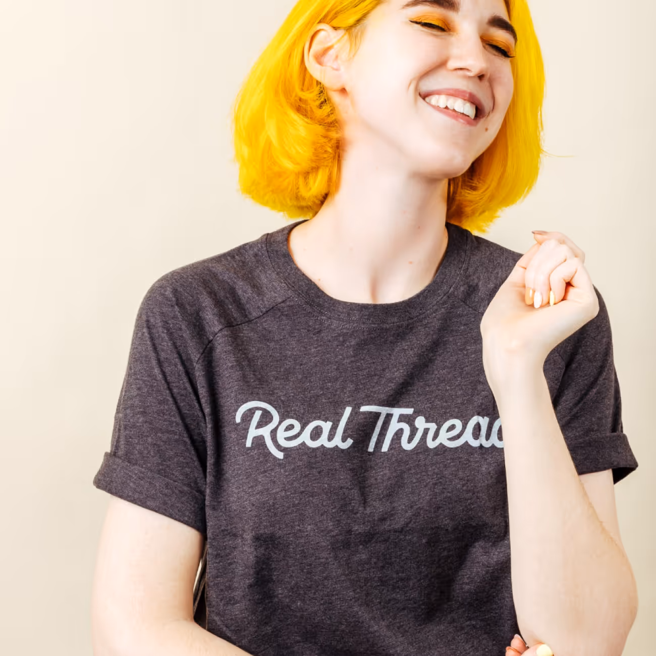 Smiling person with bright yellow hair wearing a dark gray t-shirt with the text 'Real Thread'.