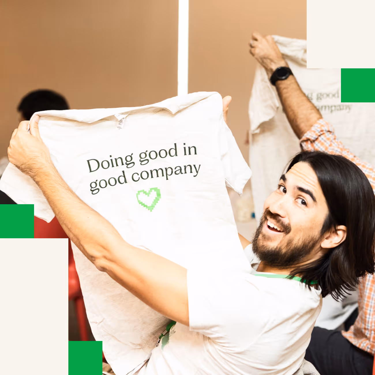 Smiling man holding up a white T-shirt that says 'Doing good in good company' with a green heart below the text.