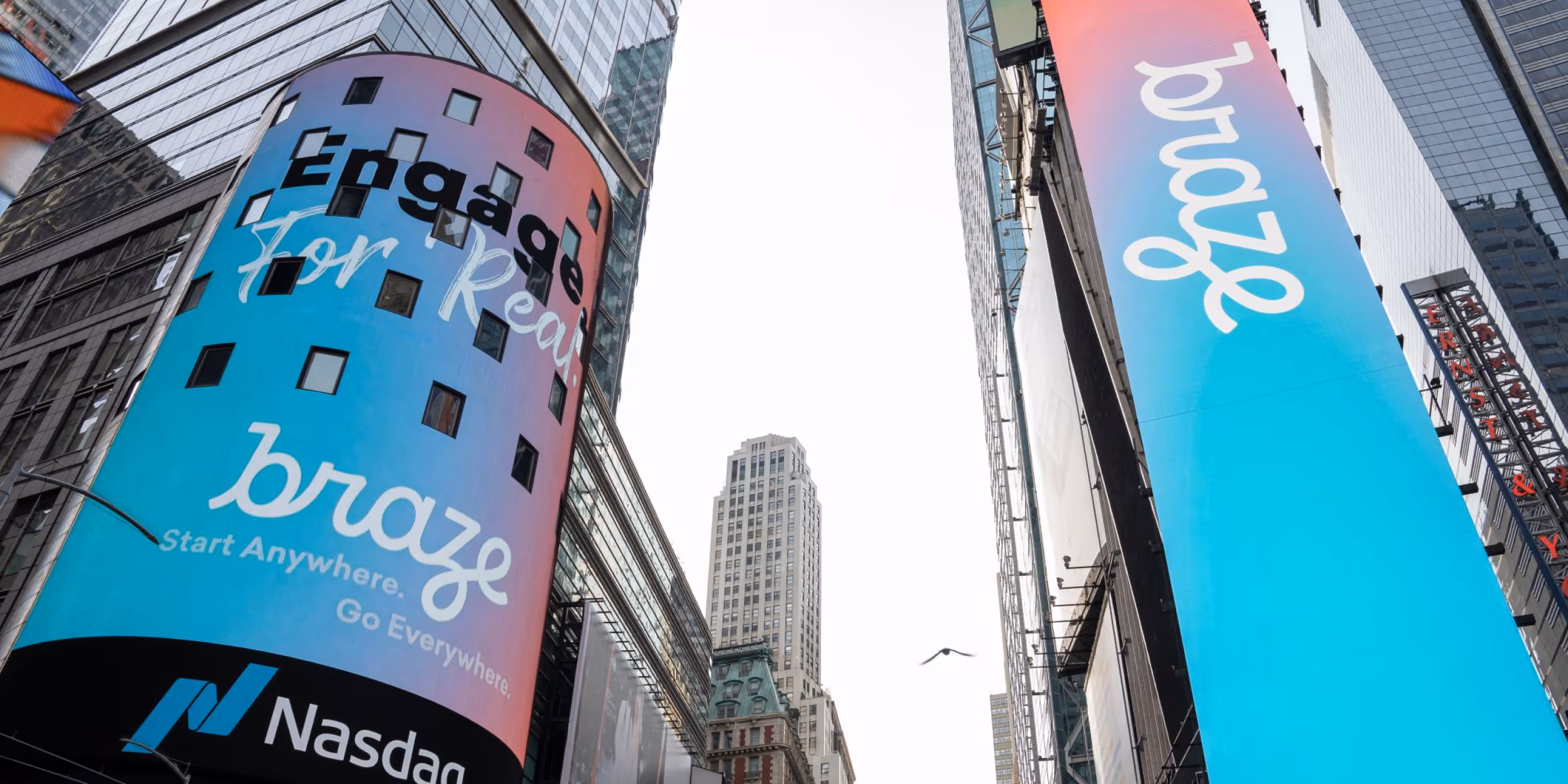 Two tall digital billboards on skyscrapers displaying colorful Braze ads including the Nasdaq logo below.