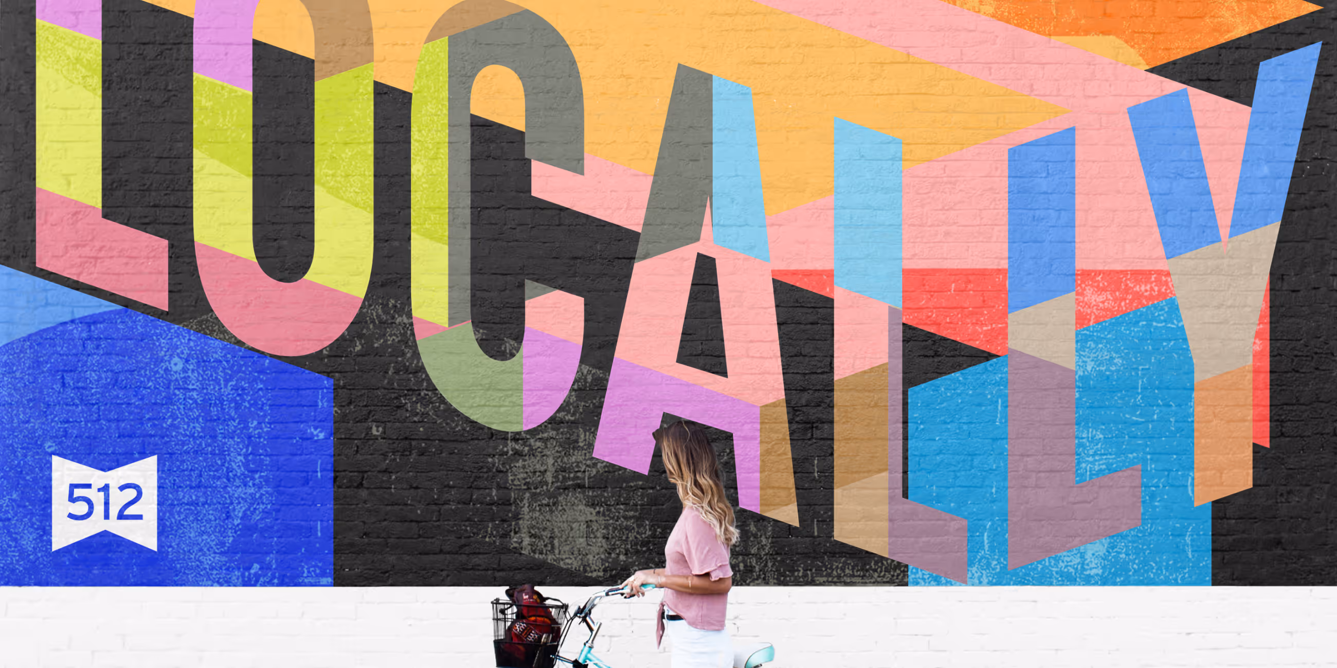 Woman with long hair pushing a bicycle past a colorful mural spelling 'LOCALLY' with geometric patterns.