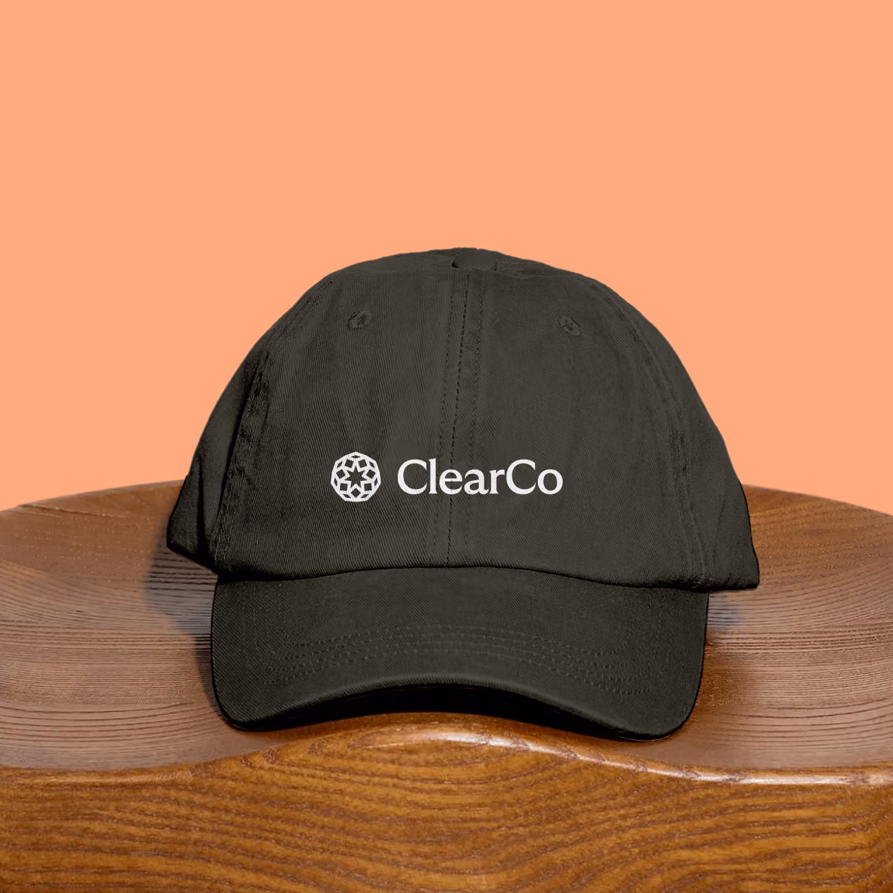 Black baseball cap with the ClearCo logo and name on the front, placed on a curved wooden surface against a peach-colored background.