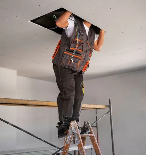 Ouvrier sur échelle, installant un plafond dans un intérieur en rénovation