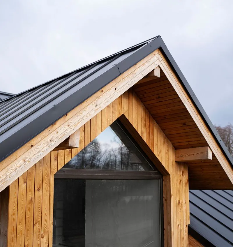 Détail architectural d'une maison en bois avec toit gris et fenêtre triangulaire