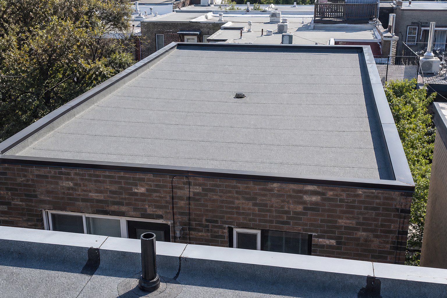 Toit plat d'un plex montréalais recouvert d'une membrane élastomère grise à granules.
