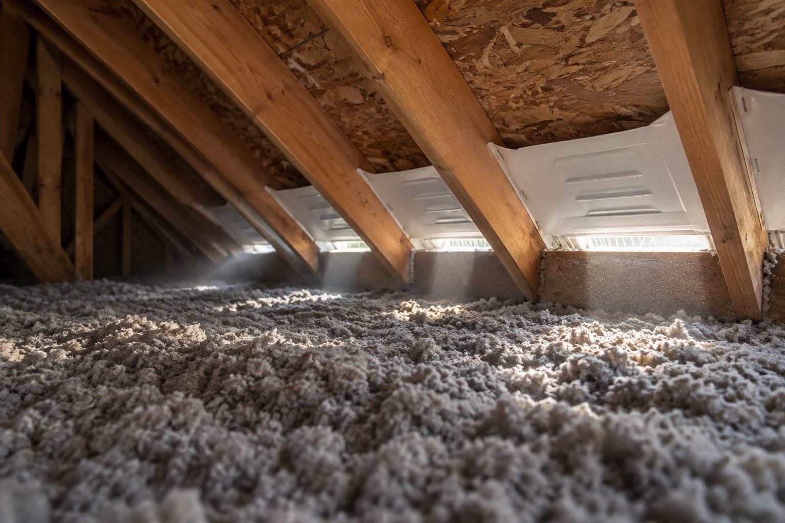 Entretoit résidentiel vu au ras du plancher, coquilles de déflecteurs blanches agrafées entre les chevrons au bas de la pente et isolant de cellulose soufflée au sol.