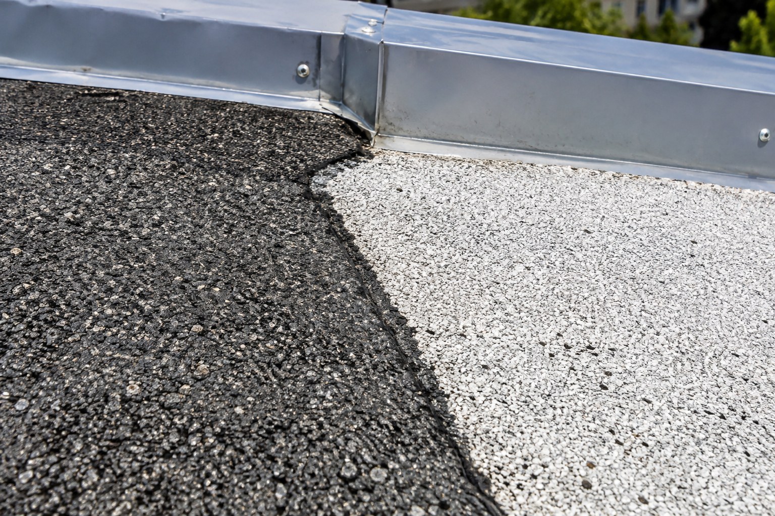 Jonction entre une vieille membrane à granules noires et une nouvelle membrane à granules pâles sur un toit plat, près d'un solin métallique.