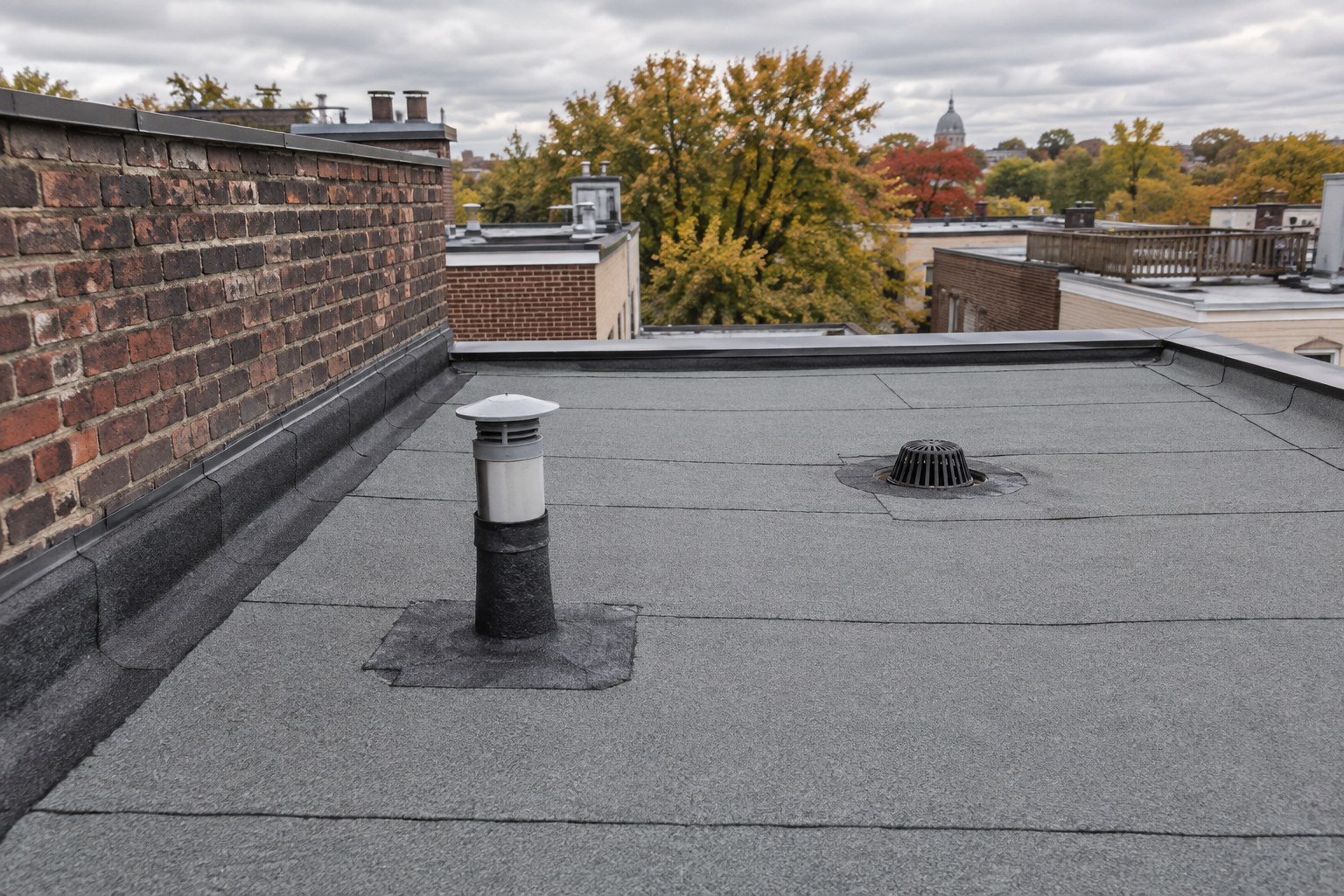Toit plat granulé d'un duplex montréalais avec solins de membrane autour d'un évent et le long d'un parapet de brique mitoyen.