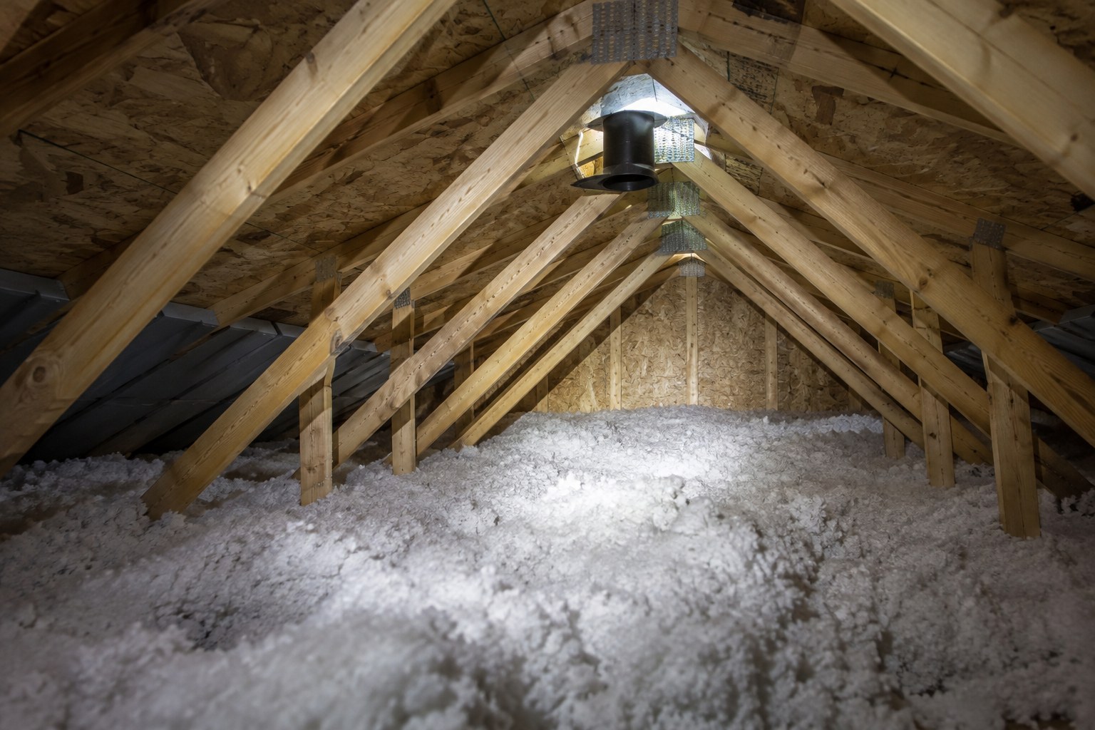 Attic with blown-in insulation between the roof trusses and a roof vent visible at the ridge.