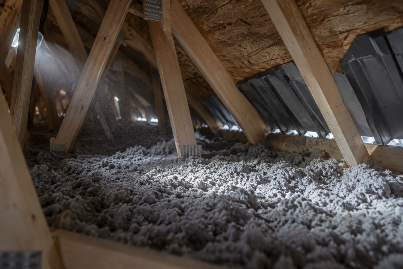 Entretoit éclairé à la lampe frontale : isolant de cellulose soufflé entre les fermes et déflecteurs de ventilation qui gardent l’entrée d’air ouverte au-dessus des soffites.