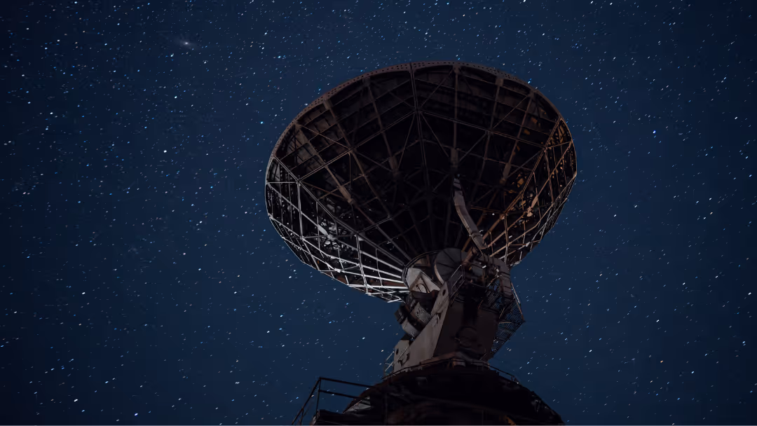 Large radio telescope dish under a clear starry night sky.