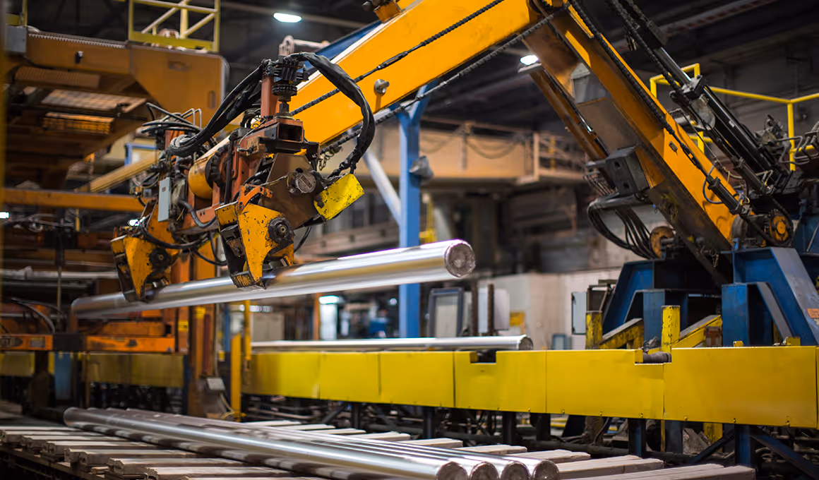 Industrial robotic arm lifting a metal cylindrical rod inside a factory.
