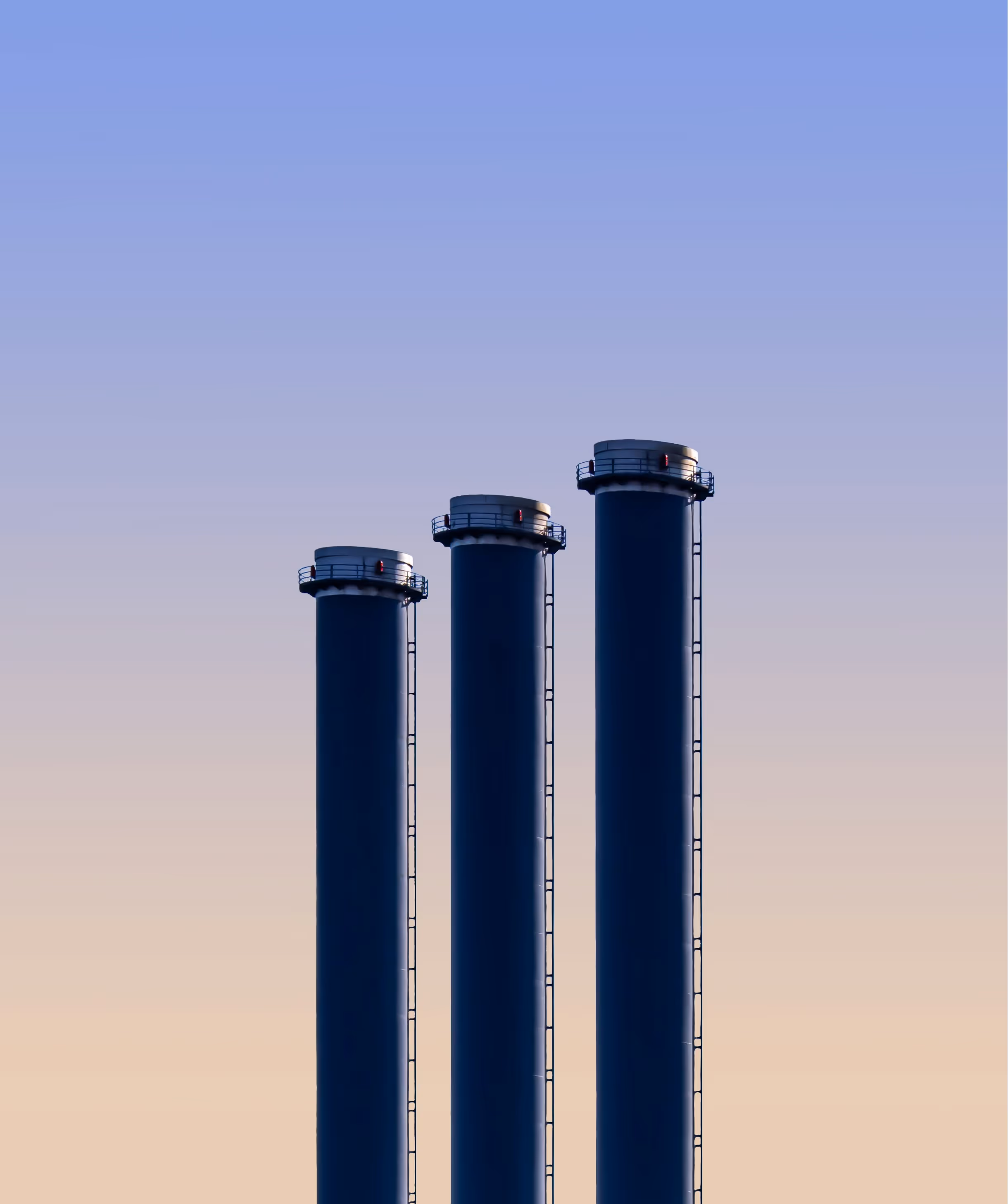 Three tall industrial chimneys of varying heights against a gradient sky at dusk.