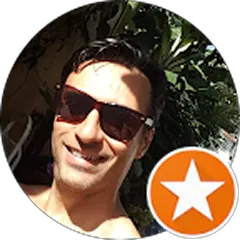 Man wearing sunglasses smiling outdoors with greenery in the background.