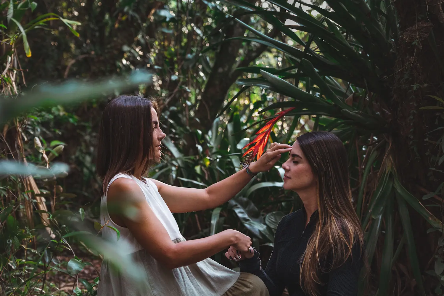 Young woman wearing headphones, writing in a notebook while looking at a tablet on a wooden table with two cups.