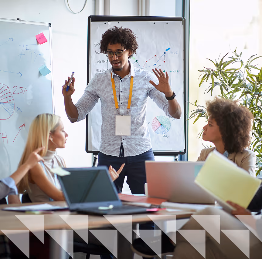 A photo of a meeting with a person explaining and presenting on a whiteboard