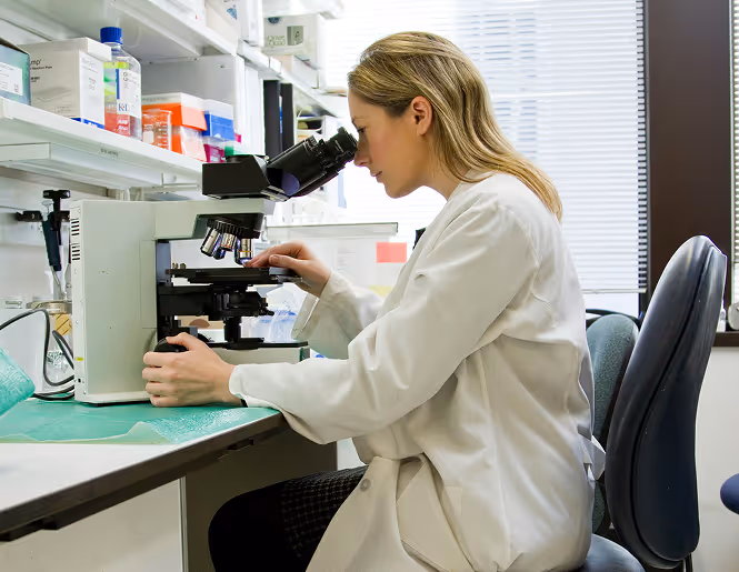 A Photograph of a medical researcher looking through a microscope