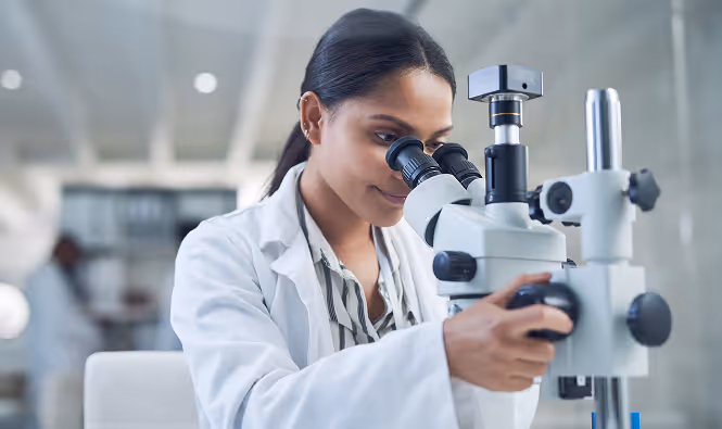 A Photograph of a medical researcher in a lab looking through a microscope