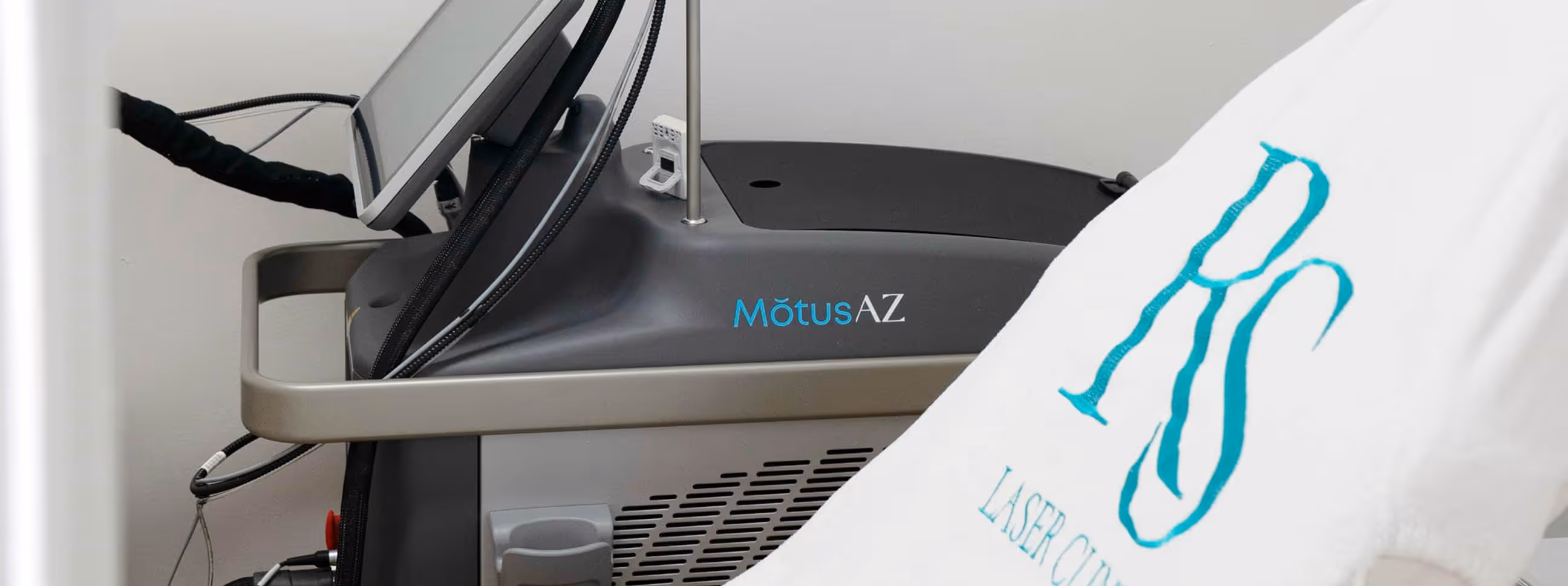 Close-up of a Motus AZ laser machine in a clinical setting with part of a white cloth embroidered with turquoise letters in the foreground.
