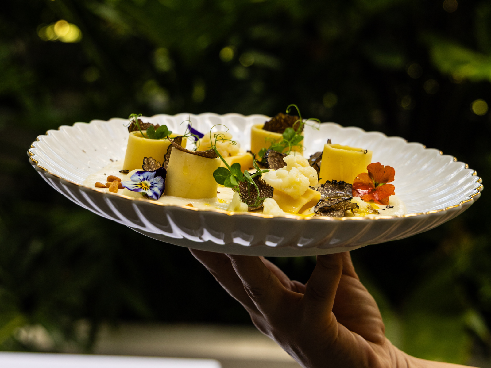 White plate with a gourmet dish decorated with edible flowers and truffle slices