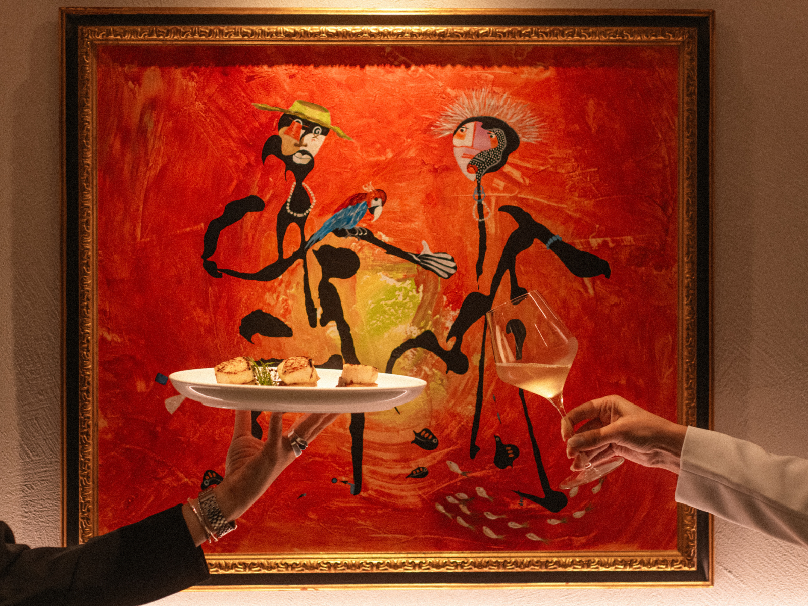 Hands holding a plate with appetizers and a wine glass in front of a red painting