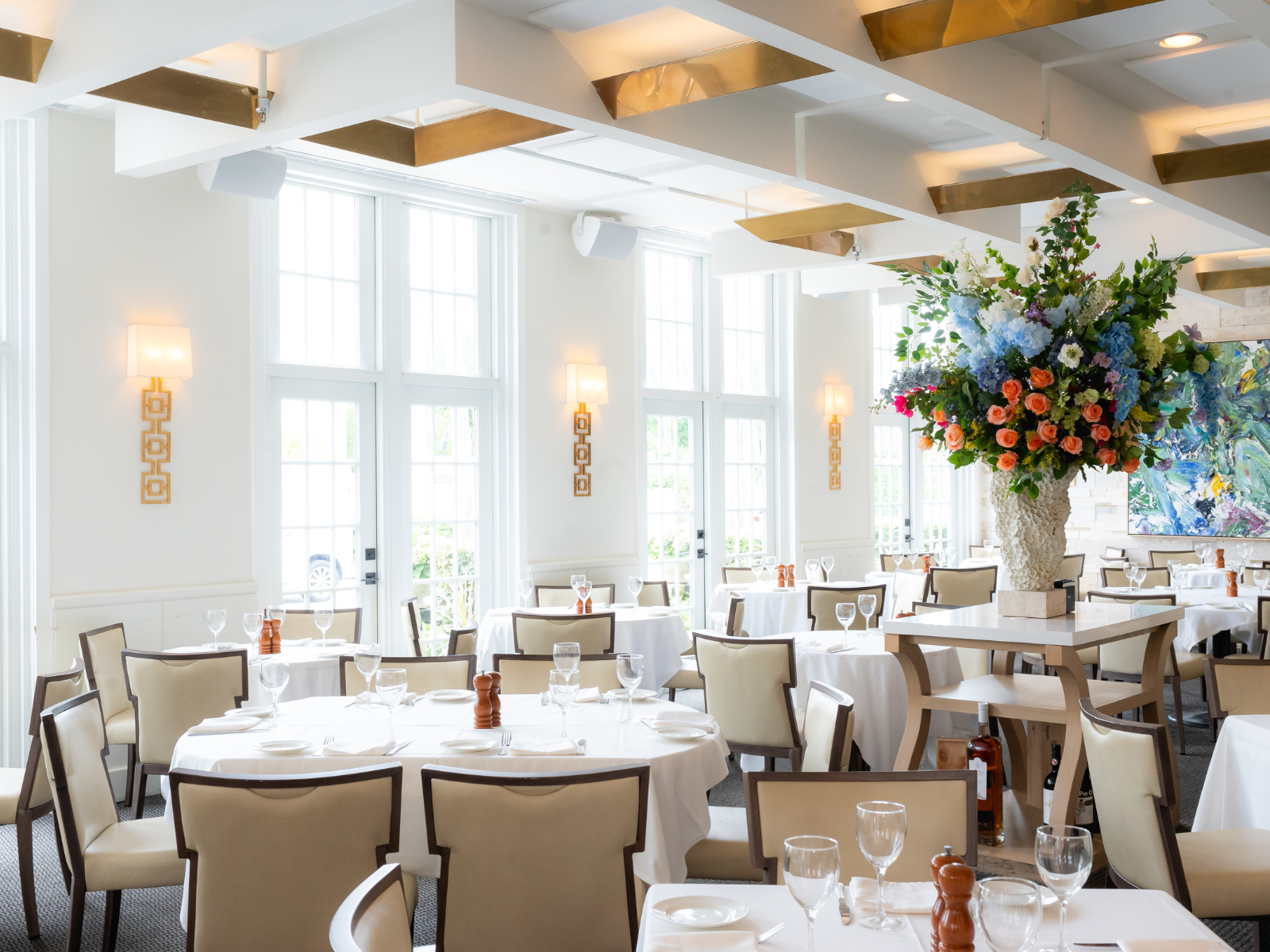 Bright restaurant interior with white tables and large flower arrangement