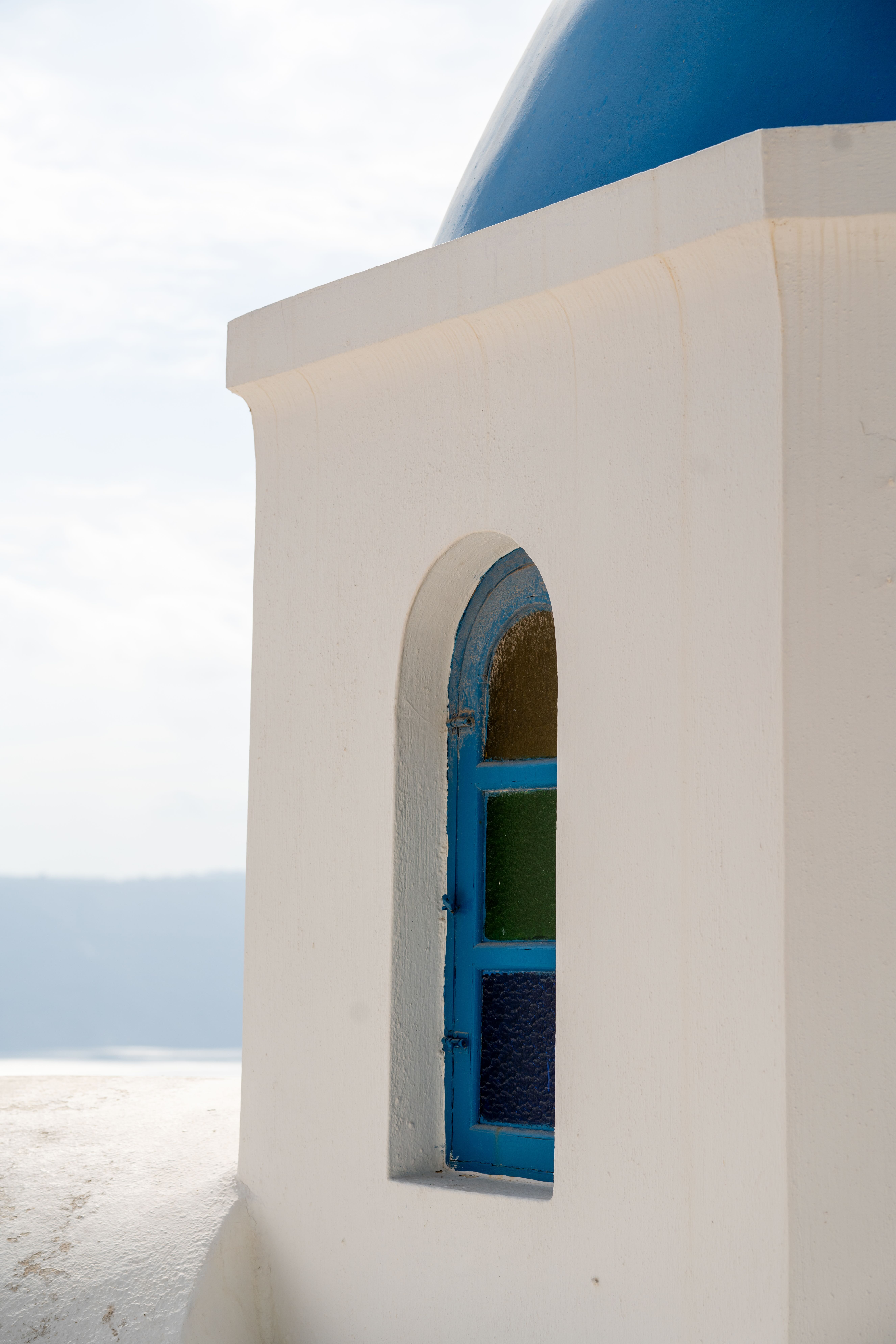 White building with blue arched window overlooking sea in Santorini, Greece