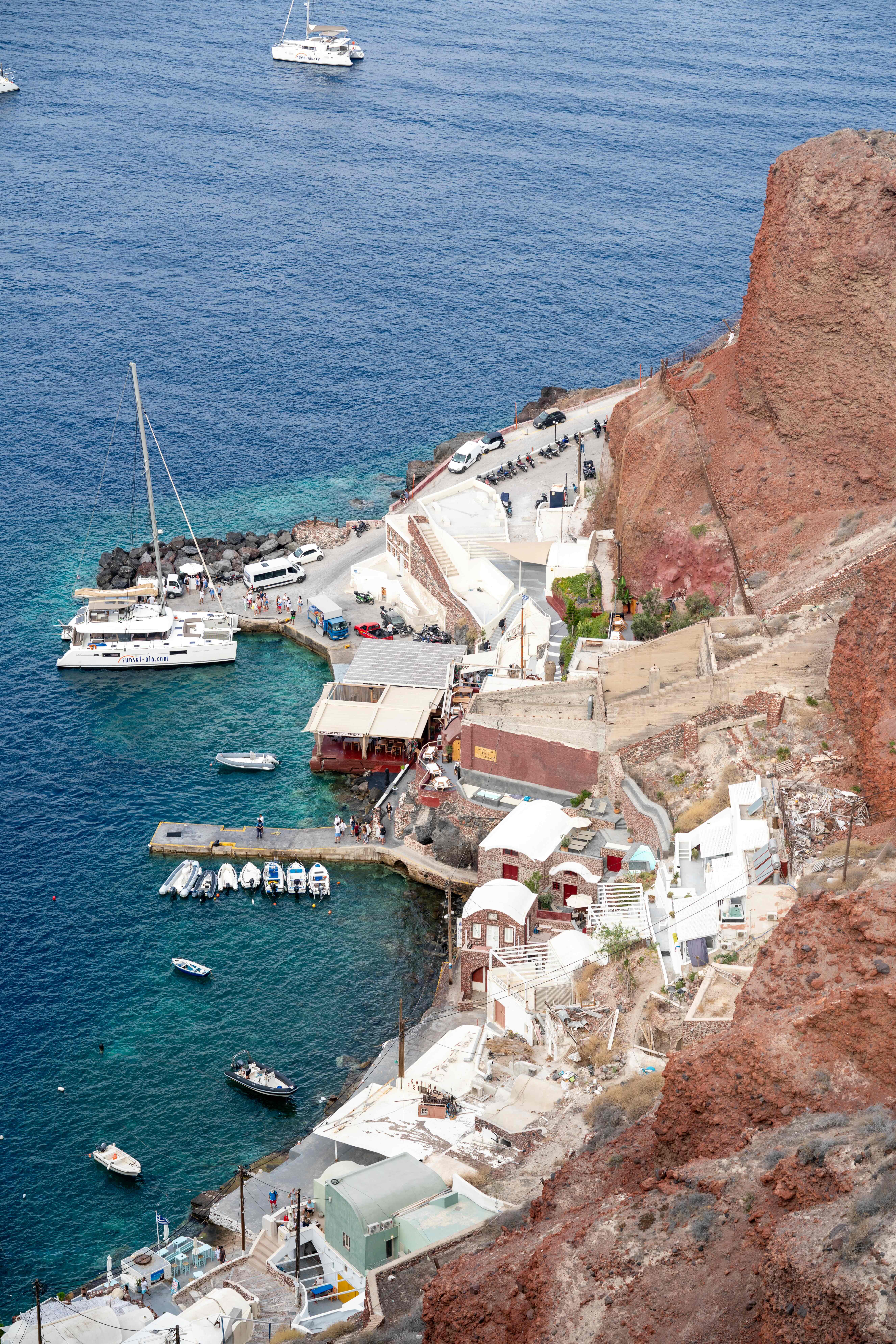 Scenic Santorini coastline with white buildings and boats against red volcanic cliffs