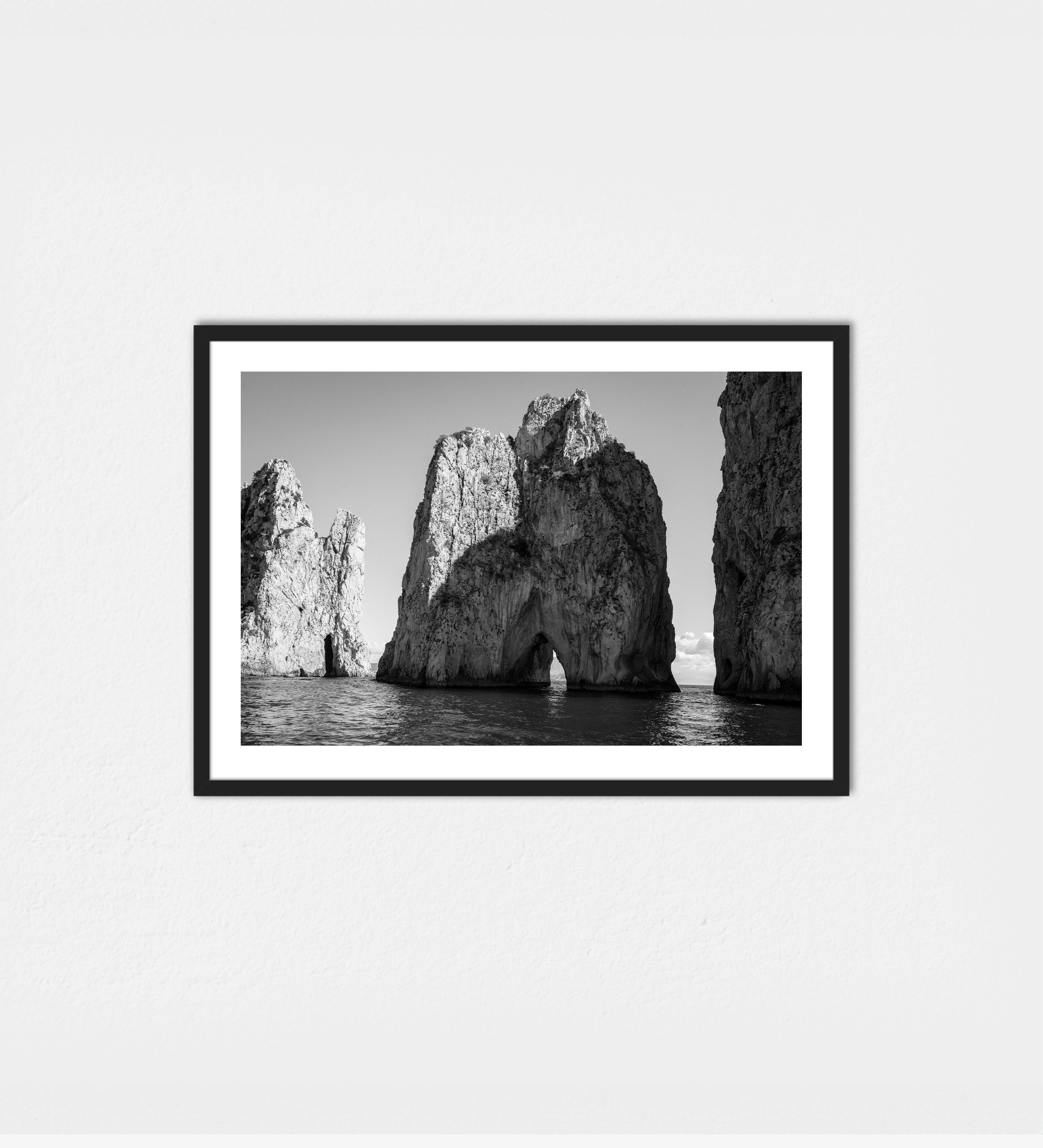 The Faraglioni off Capri, their sunlit cliffs rising above calm turquoise water — in black and white.