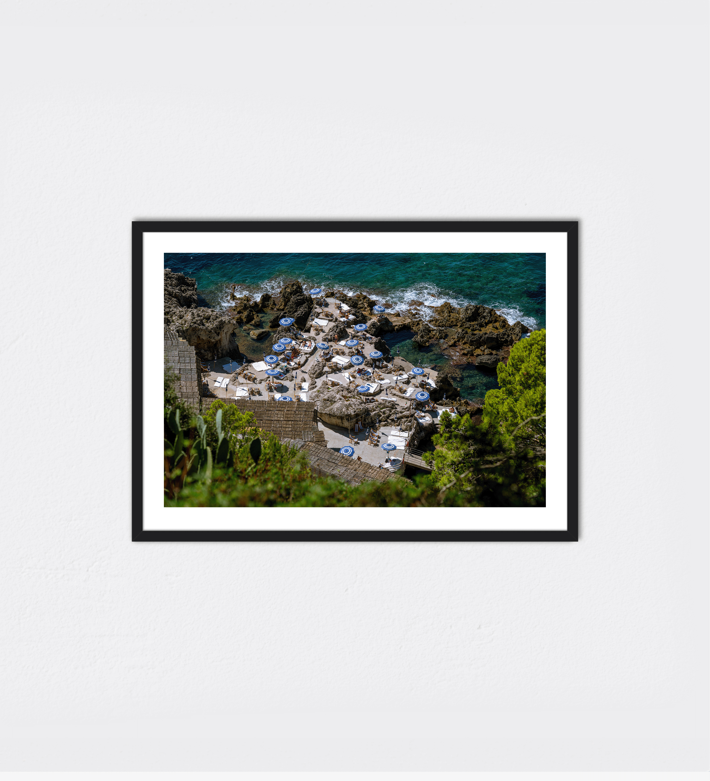 White sunbeds with blue umbrellas line the natural stone platforms above turquoise.