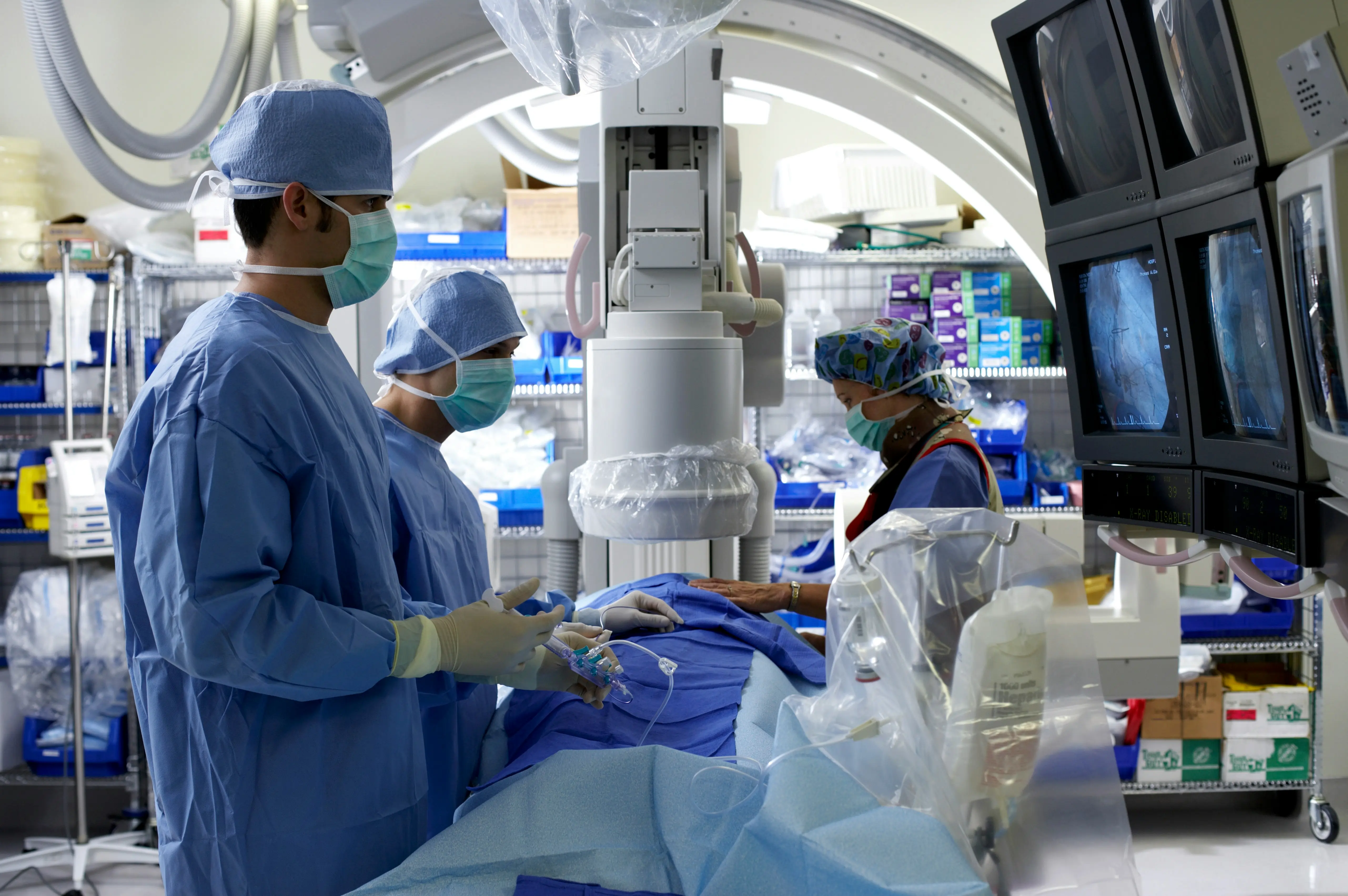 A surgery team standing over a patient during a procedure, surrounded by machines.