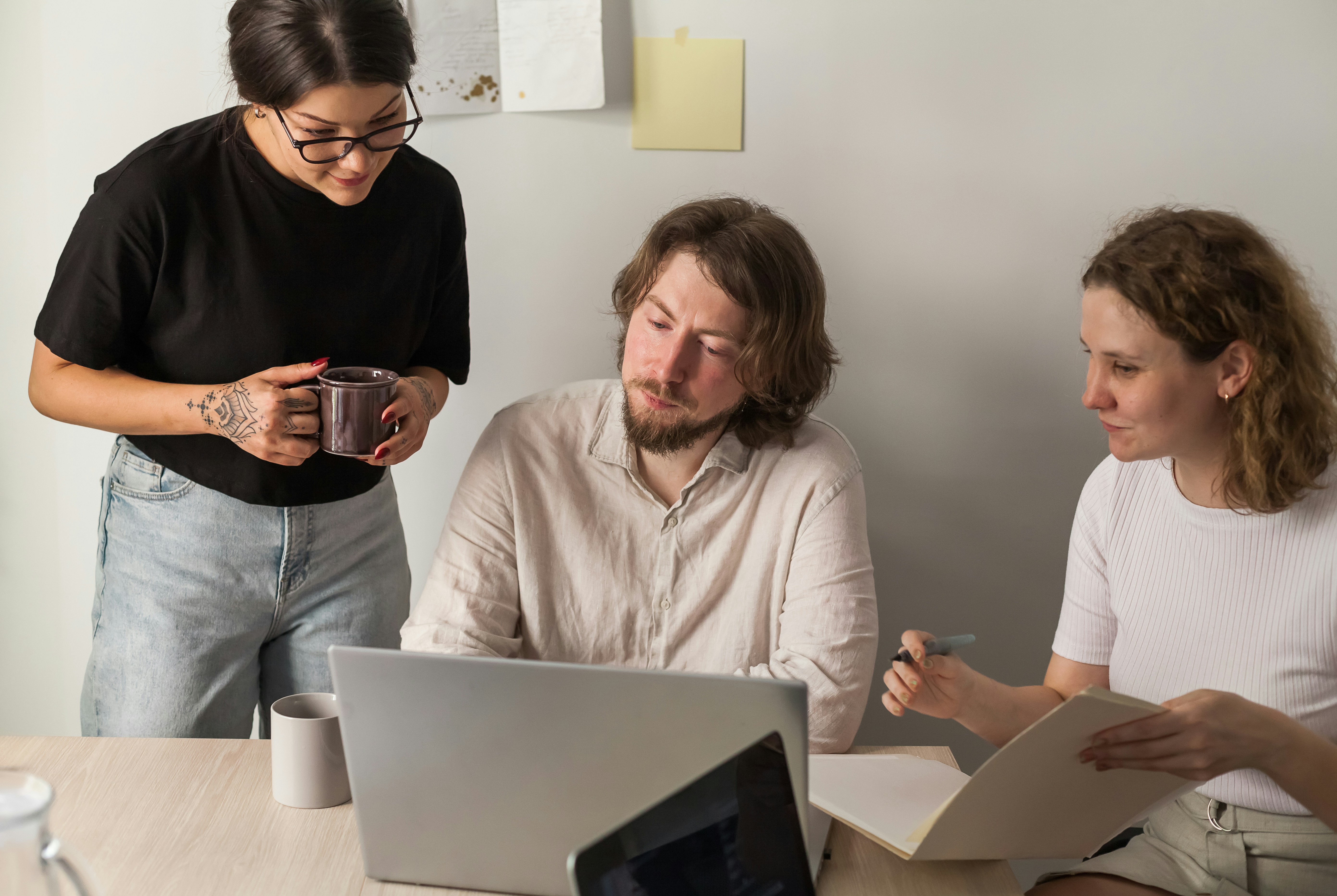 3 individuals look at a computer screen and take notes; one is standing.