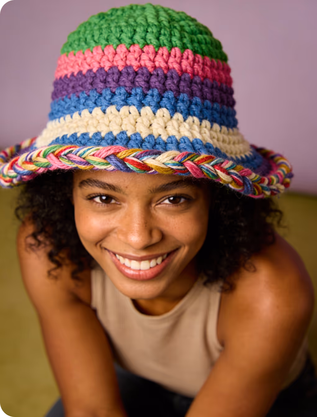 Smiling woman wearing a colorful striped crochet hat with a braided brim.
