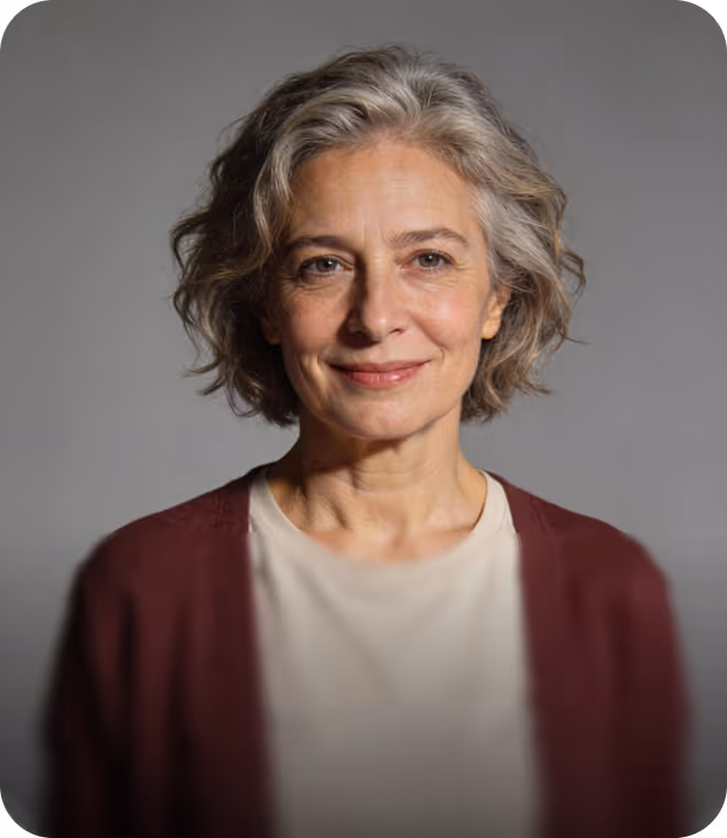 Smiling middle-aged woman with wavy gray hair wearing a white top and maroon cardigan against a plain gray background.